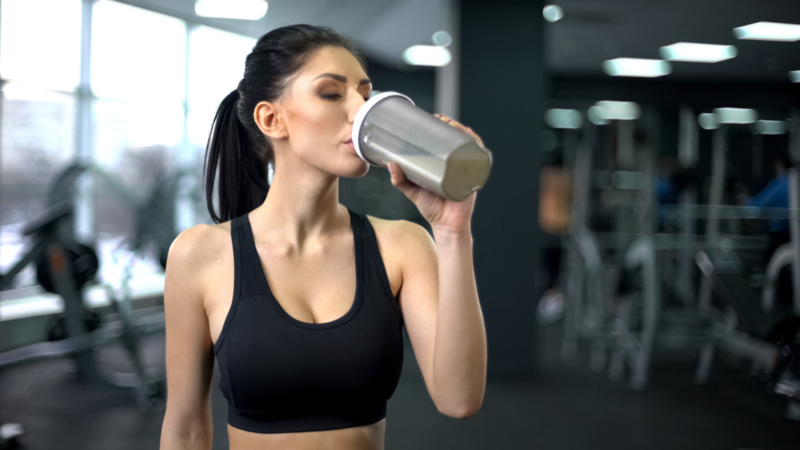 Sporty woman drinking protein shake after workout, muscle gain nutrition, health