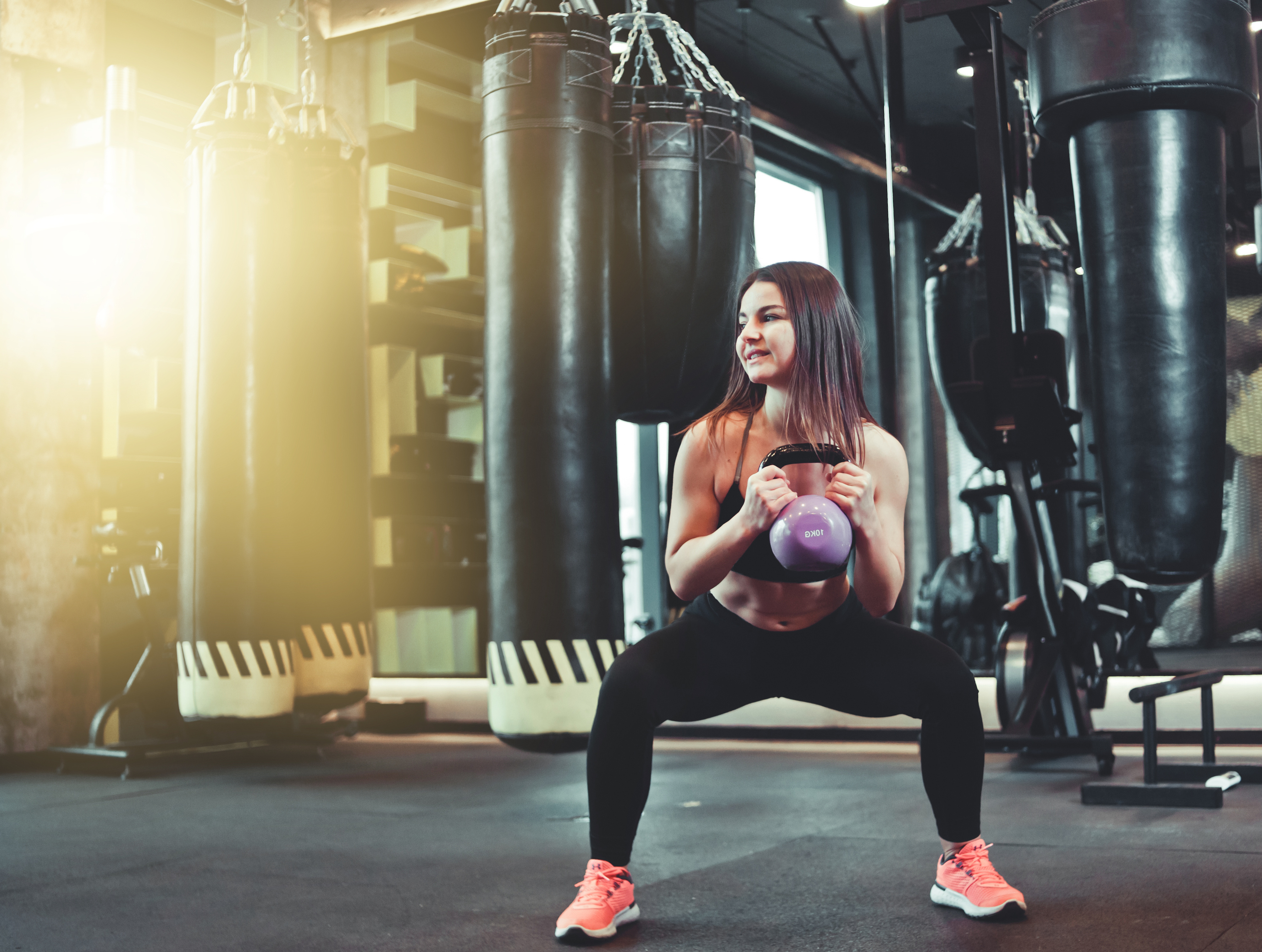 Functional training. Woman doing squats exercise with kettlebell indoors at gym